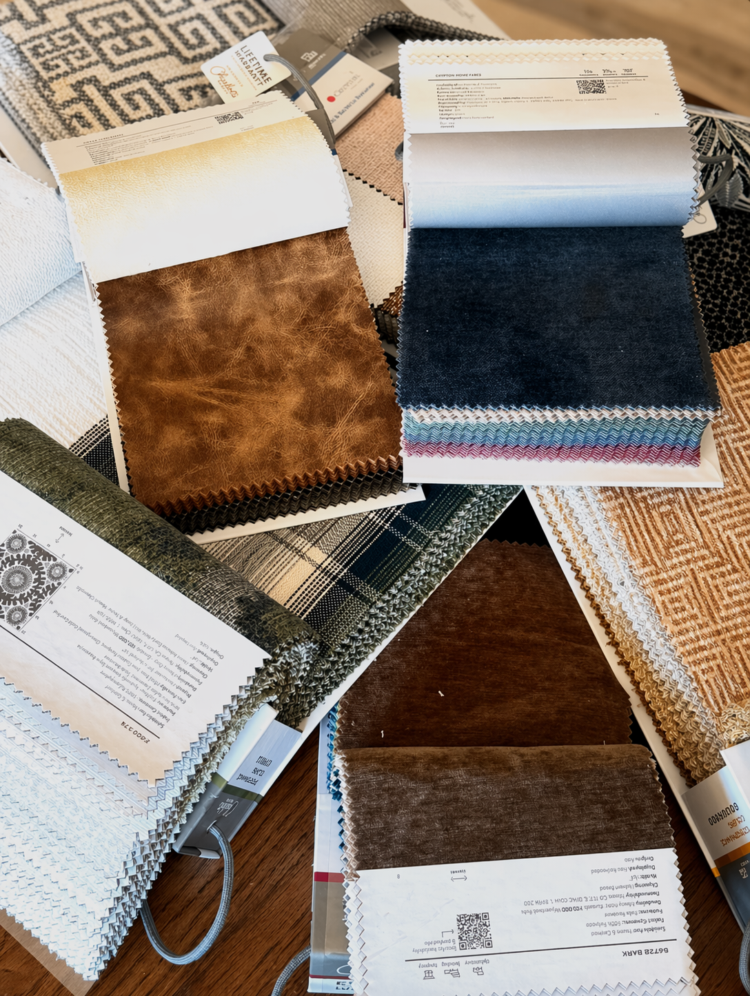 An array of fabric and leather swatches — velvet, plaid, herringbone, and aged leather — laid out across the studio table
