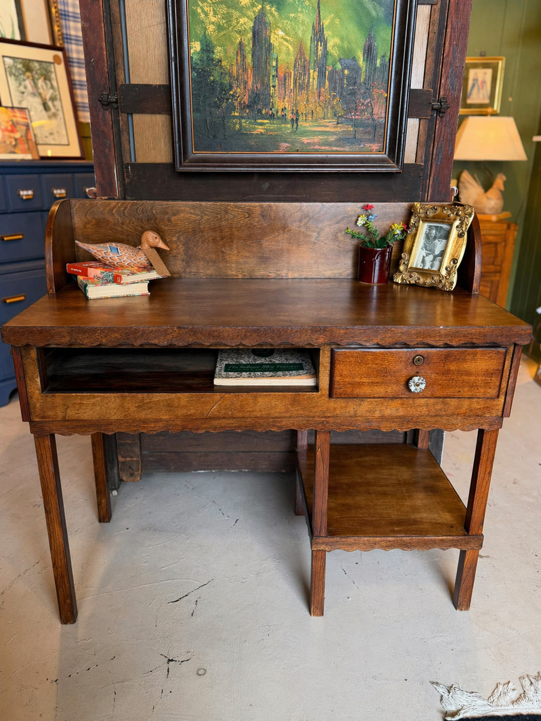 Restored oak writing desk with scalloped apron, single drawer, and lower shelf styled with books and decor